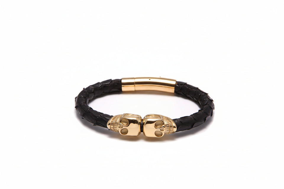 Black leather bracelet with gold skull clasp on a white background