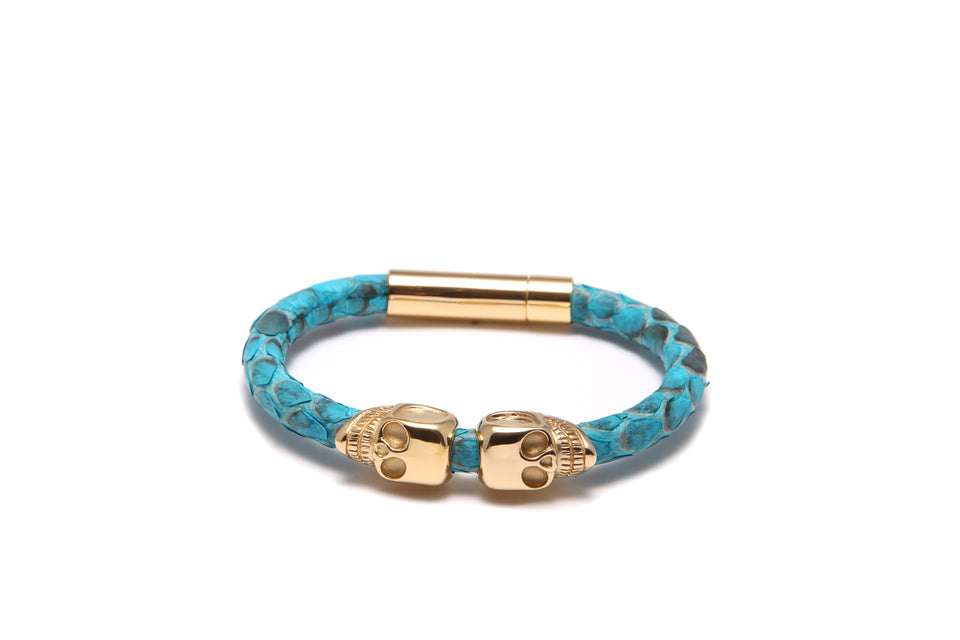 A turquoise blue and gold python leather bracelet with a skull shape design.