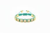 Green braided bracelet with gold square beads on a white background